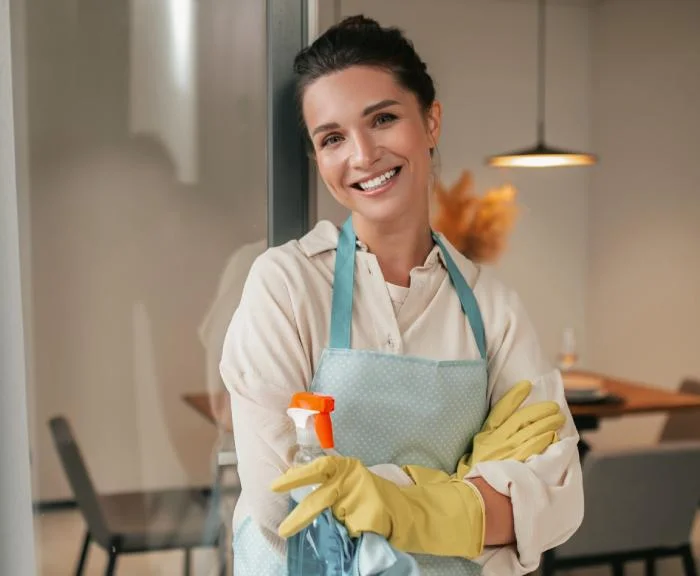 Cleaner wearing gloves and holding a spray bottle and cloth in a furnished interior