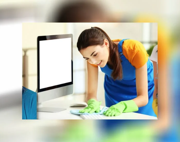 Cleaner wiping a computer keyboard and desk with a cloth while wearing gloves