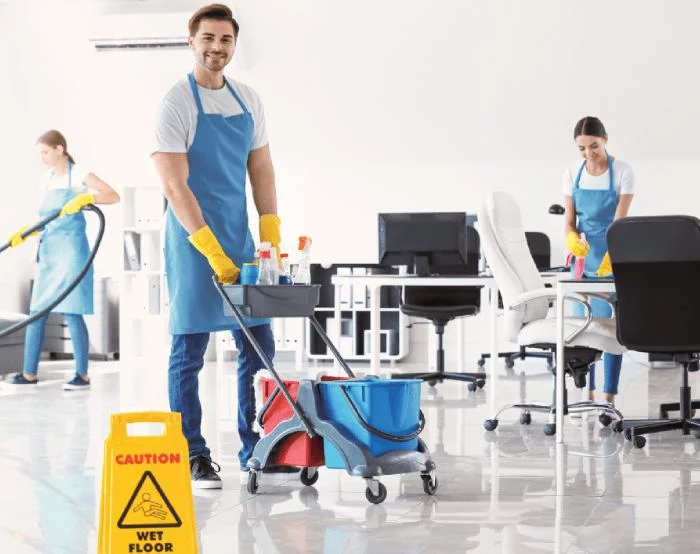 Commercial cleaners mopping and vacuuming an office with a wet floor warning sign
