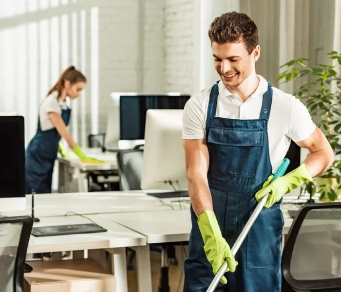 Two cleaners wiping desks and mopping the floor in a modern office